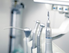 Close-up of various dental instruments in a dental clinic, with a focus on a metal dental drill. The background is blurred, highlighting the clean, clinical setting.