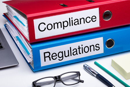 Ring binders labelled “Compliance” and “Regulations” on a desk.