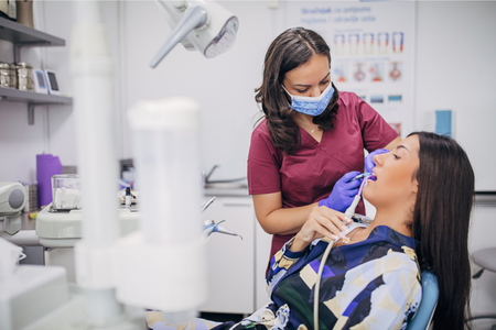 A dentist treats a female patient reclined in a dental chair inside a modern dental clinic.