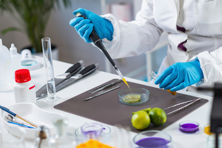 Laboratory technician wearing protective gloves using a pipette to handle samples on a lab bench.