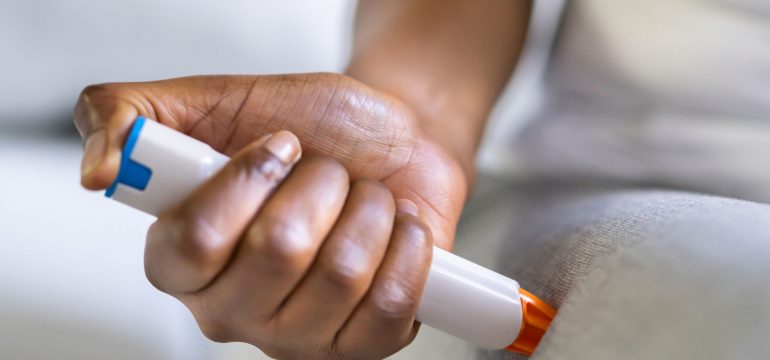 a person holding and injecting an AAI (Auto Adrenaline Injection) with their right arm onto their right leg