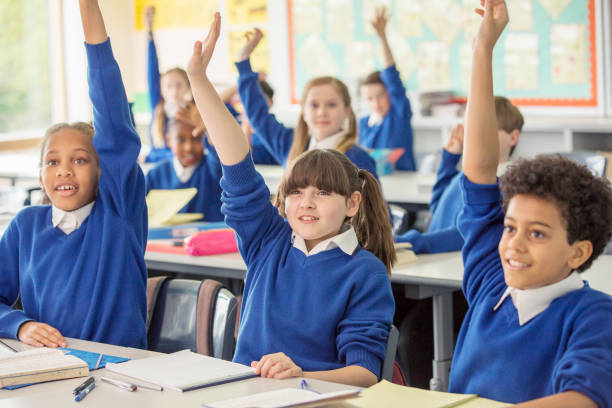 a classroom full with school pupils raising their hands